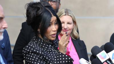 Cardi B speaks to reporters outside court. She has black hair tied up and wears a black top with white polka dots