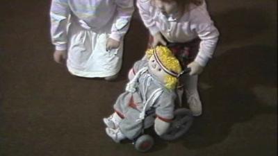 Two children play with a doll in a wheelchair