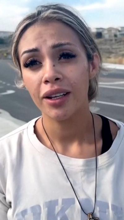 A woman in a white sweatshirt looks into the camera while speaking.