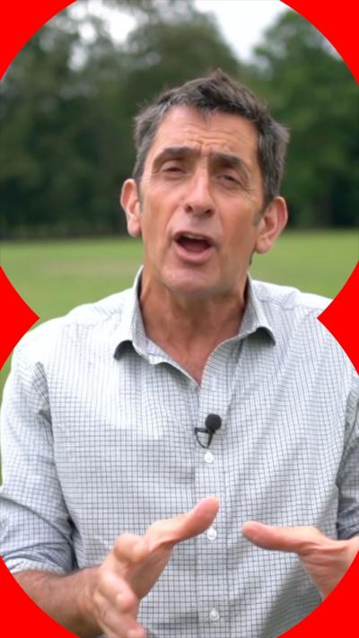 A man with short, dark grey hair wearing a shirt talks to the camera