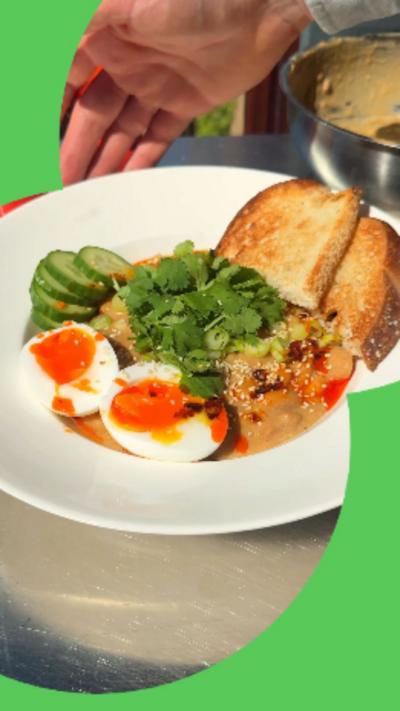 A bowl of butter beans in sesame sauce, garnished with coriander cucumber, a soft-boiled egg and toast.
