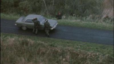 Two soldiers standing next to a car on a rural road.