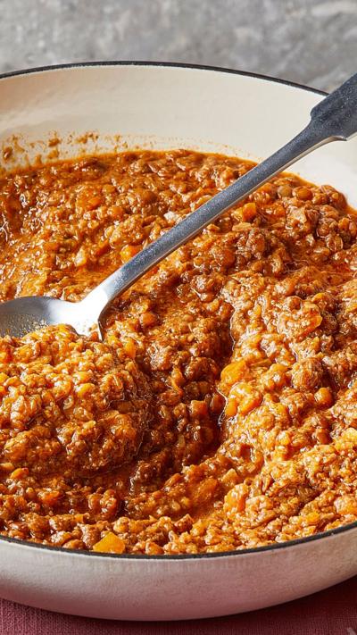 A white bowl with lentil ragu and a serving spoon sitting in it