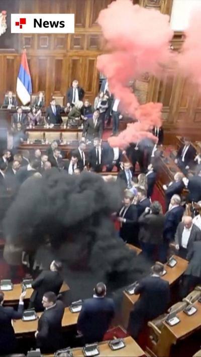 Pink and grey smoke billows in a chaotic scene inside Serbia's parliament.