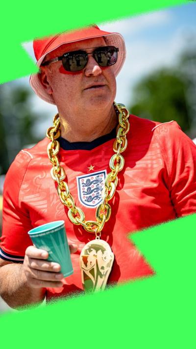 A man wearing an England shirt, bucket hat, sunglasses and a chunky golden necklace with a World Cup pendant holds a paper cup in the sun.