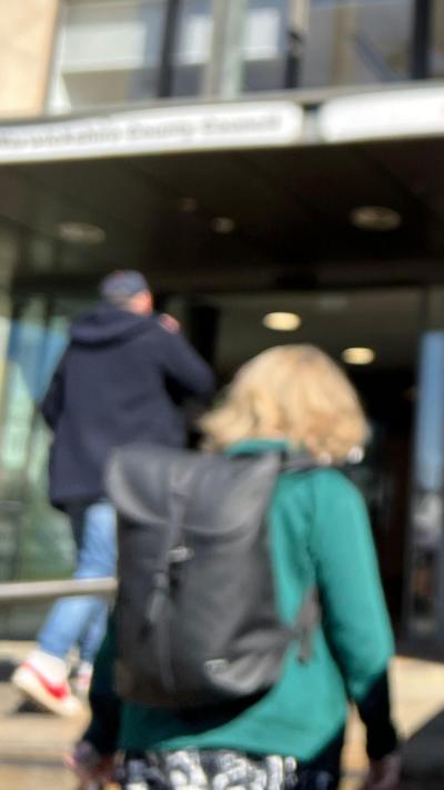 A blurred image of a man and woman walking into a council office. The man has a blue coat, the woman has a green coat and black rucksack