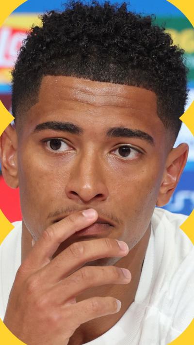 Jude Bellingham wears a white t-shirt and puts hand up to chin.