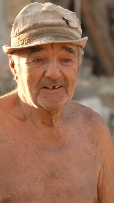 A shirtless elderly man wears a hat and speaks to the BBC after losing his home in Russian airstrikes