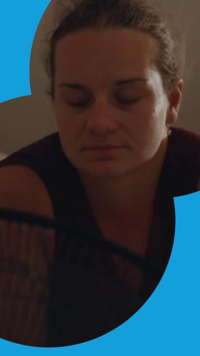 A woman sits on a bed in front of a fan