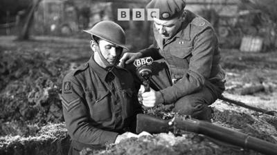 A man in a uniform, holding a ˿ microphone, interviews a soldier