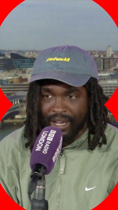 A man with shoulder-length dark hair talks into a microphone