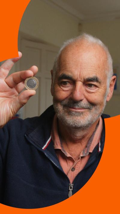 Man smiling whilst holding a coin in his hands