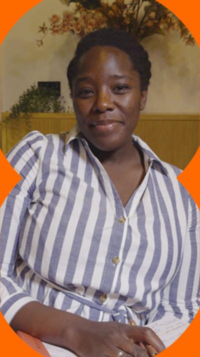 Kimberley Wilson sat in a white and blue striped shirt. She's smiling and holding a notepad and pen.