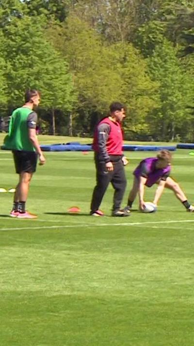Rugby players wearing different colour bibs are in training on a sunny day.