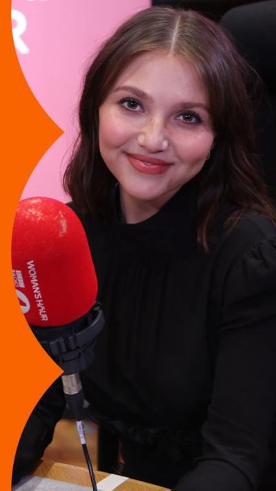 Mia McKenna-Bruce has long brown hair and wears black, and sits in the Woman's Hour studio