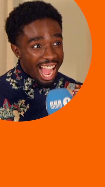 Caleb McLaughlin has his mouth open in excitement. He has short black hair and wears a blue shirt with multicoloured patterns