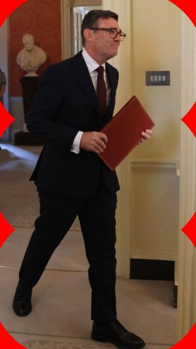 Andy Burnham walking, holding a red folder and wearing a dark suit