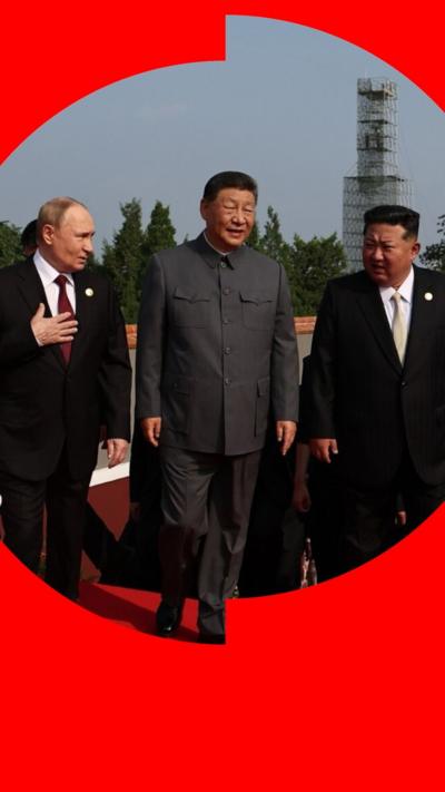 Vladimir Putin, Xi Jinping and Kim Jong Un walk alongside each other on a red carpet. Putin and Kim wear two piece black suits, while Xi wears a buttoned up grey suit