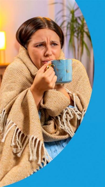 A woman looking cold, with a beige blanket around her holding a blue cup.