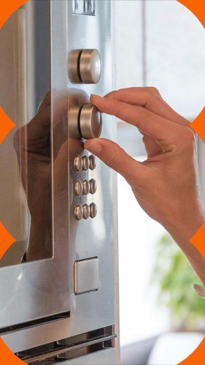 A stainless steel microwave, with a woman's hand turning one of the dials, in a white kitchen.