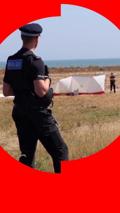 A police officer looking at another officer on the beach, next to a forensic tent
