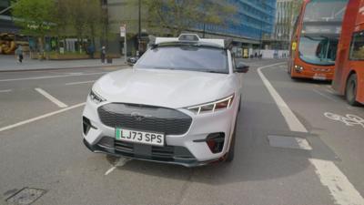 A driverless car on a road in London - there are two red buses to the right