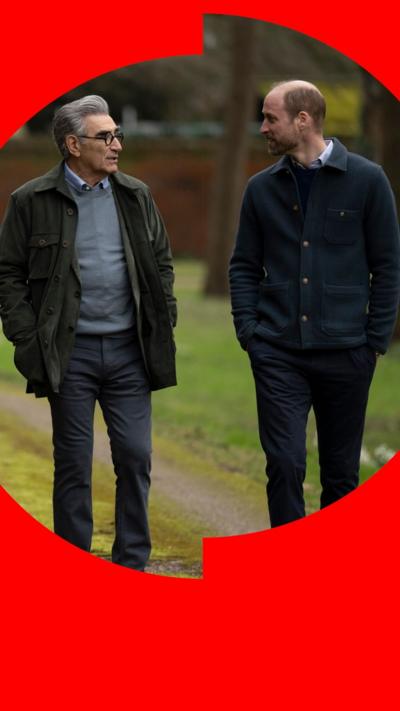 Eugene Levy and Prince William along a mossy path followed by a black spaniel.
