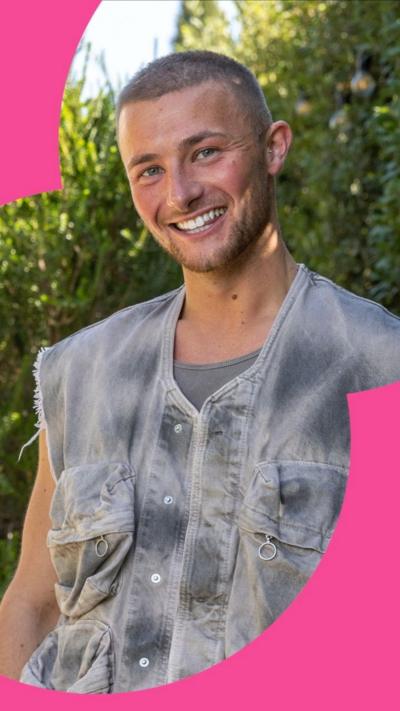 Man in grey sleeveless jacket smiling at the camera 