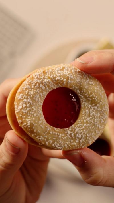 Hands hold a round biscuit with red jam in the middle