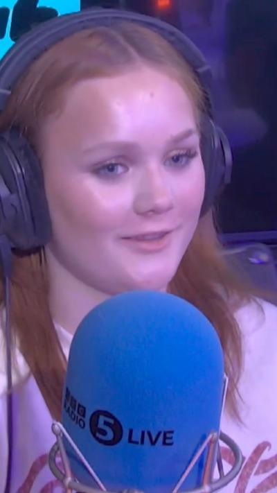 A young woman with long dark hair sits in front of a blue microphone