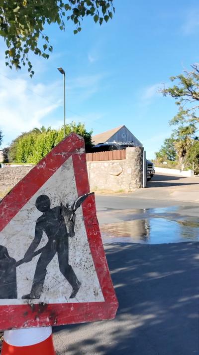 A road with a puddle in the middle There is a workers sign. 
