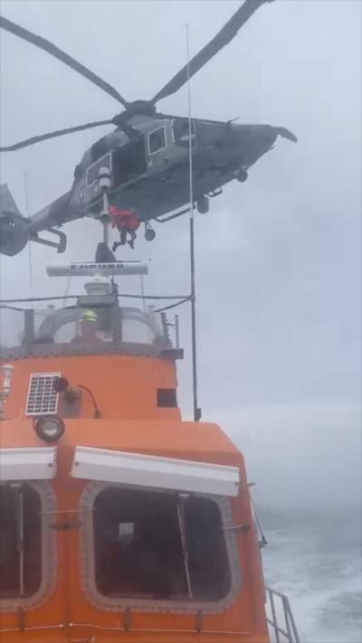 An orange lifeboat sailing with a grey helicopter flying above 