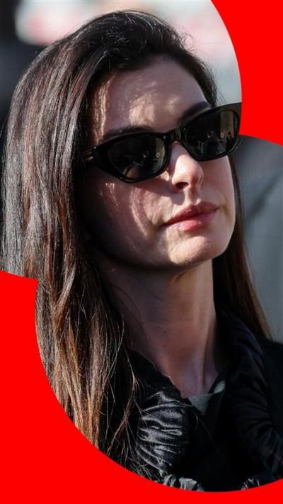Anne Hathaway has long brown hair and wears sunglasses. She looks sombre 