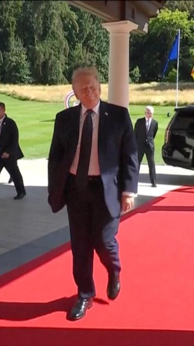 President Trump wears a blue suit, white shirt and blue tie as he walks down a red carpet in France.