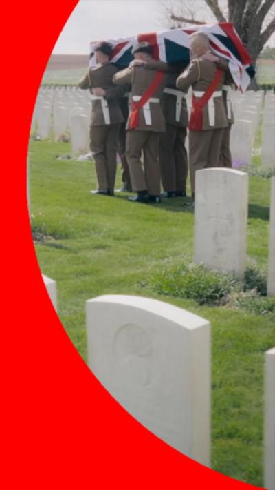 Men in British services uniforms carry a coffin, draped in the Union Jack, through a war cemetery.