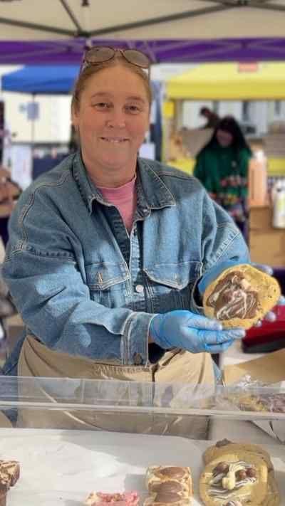 Woman with glasses on her head holds a cookie at a farmers' market stall.