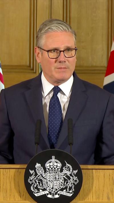 UK PM Keir Starmer speaking at podium and standing in front of two union jacks