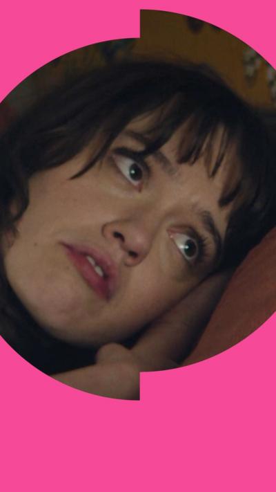 Aimee Lou Wood lying down in bed with her head on the pillow looking at her sleeping partner