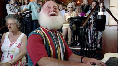 Buster Merryfield singing and playing piano.