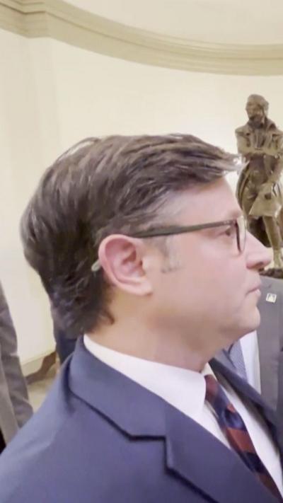 Mike Johnson's side profile as he wears glasses and a blue suit as he addresses reporters.