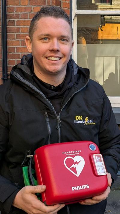 A man stands holding a defib