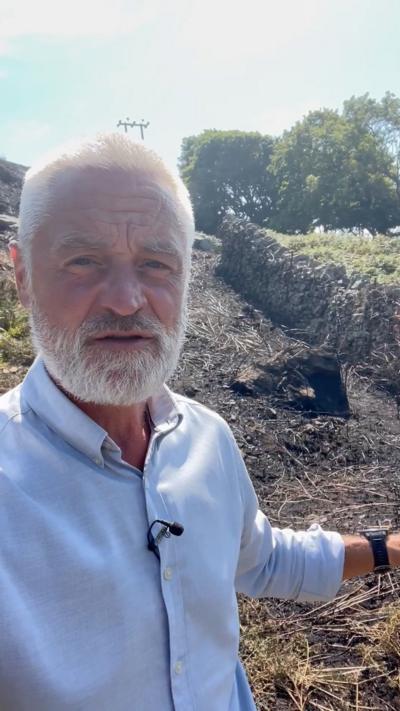 Brendon Williams, who has short grey hair and a beard, stood in front of scorched earth in the sun