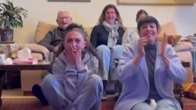 Family member cheer and clap while sat in living room seeing hostages released