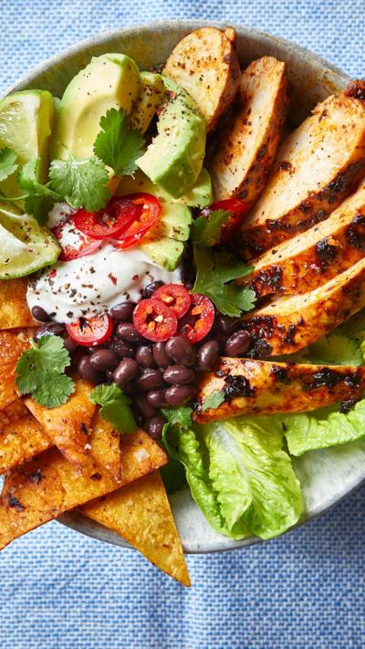 Top down view of sliced chicken, avocado, tortilla chips and salad
