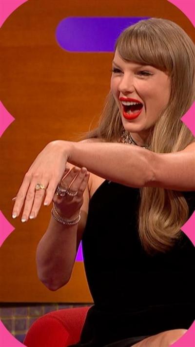 Taylor Swift smiles while holding out her left hand to show her engagement ring