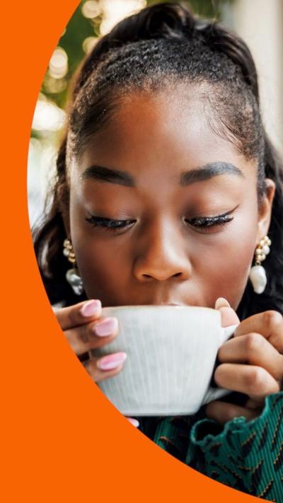 Front view of a woman with pink nails and green jacket sipping from a white cup.