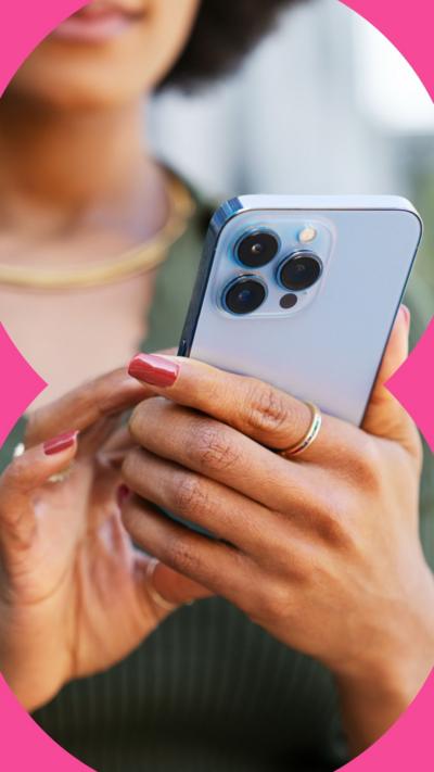 A woman wearing a green top is holding a light blue mobile phone in her hand and using her other hand to press on the screen.