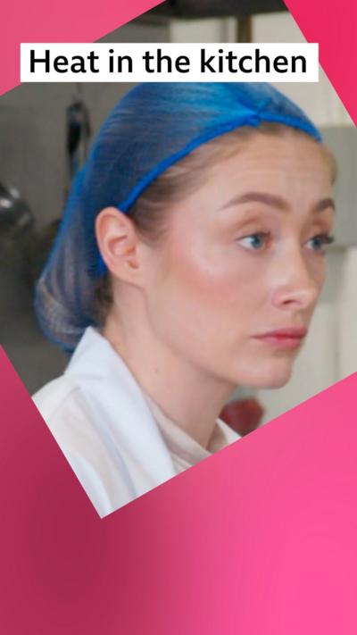 A stressed looking woman wearing a blue hairnet in a kitchen