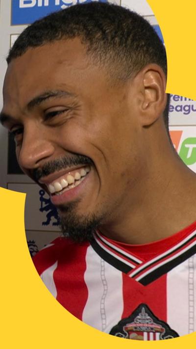 Two footballers stand for post-match press conference. One, Wilson Isidor, smiles as he looks at the interviewer