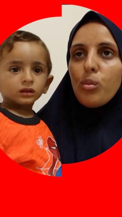 A mother holds her child - she wears a black headscarf, he wears orange Spider-Man pyjamas 
